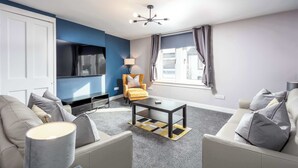 Un salon moderne comprenant un canapé, un fauteuil, une table basse, un téléviseur et une lampe.
