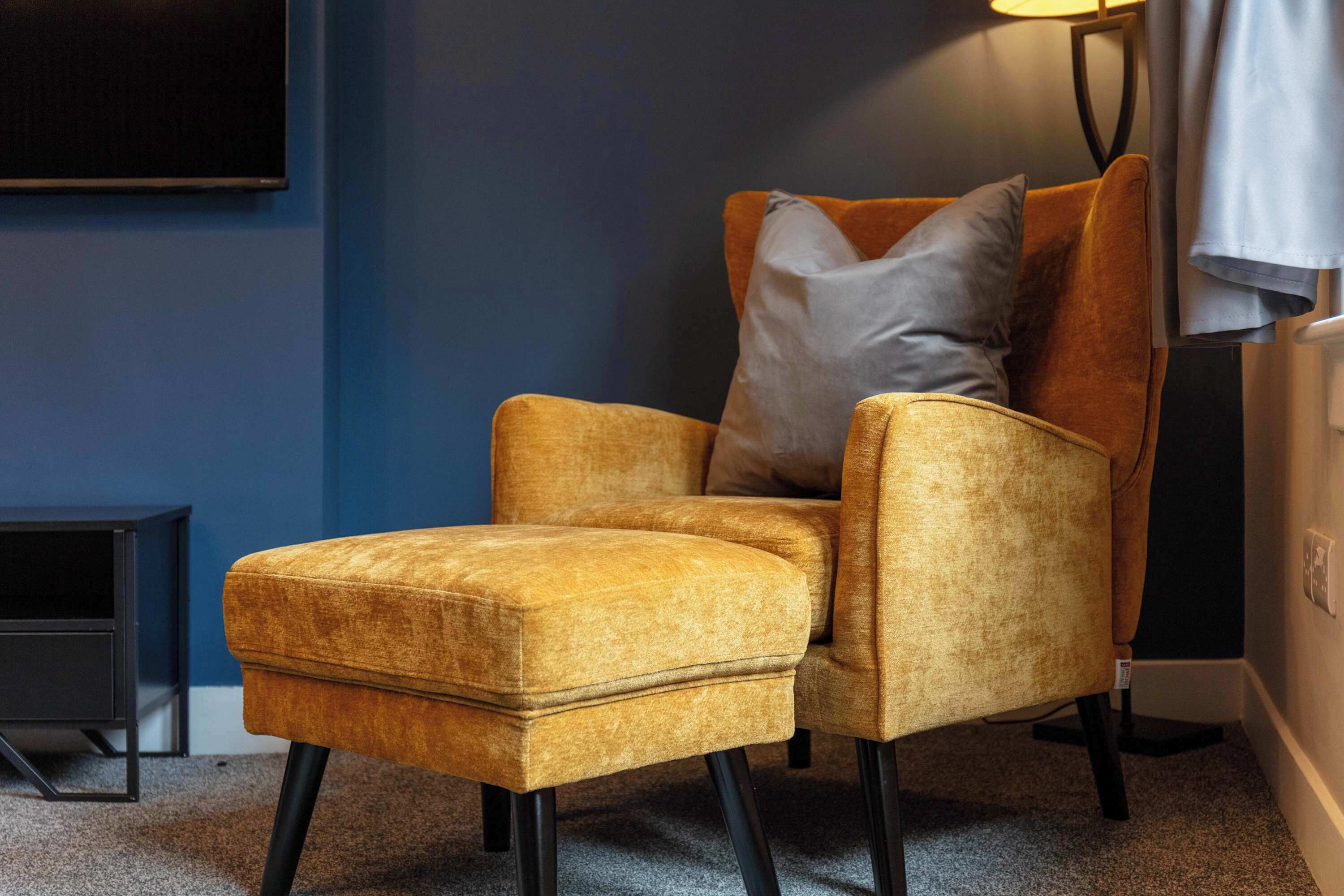 A room with a single armchair, a small side table, and a wall-mounted TV.