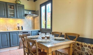Comedor con una mesa dispuesta para cuatro, armarios de cocina, una ventana y una pared de piedra.