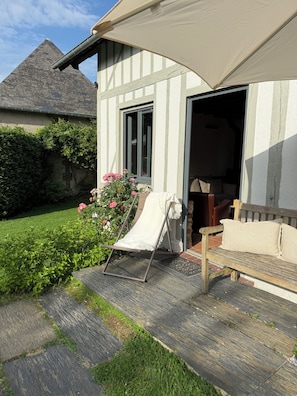 Une maison avec un jardin, un banc en bois, une chaise et un grand parasol.