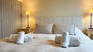A neatly made bed with pillows and rolled towels, two bedside tables with lamps, and a sloped ceiling.