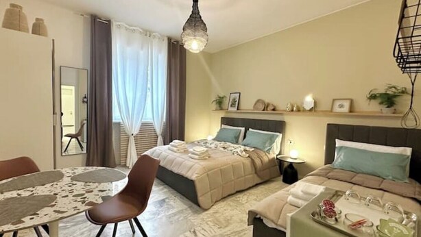 Habitación de hotel con cama, mesita de noche, silla, mesa y lámpara colgante.