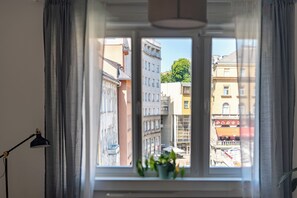 A window with a view of multi-story buildings, a potted plant on the windowsill, and a lamp on the left. - Wally apartments by Flat White (Zagreb)