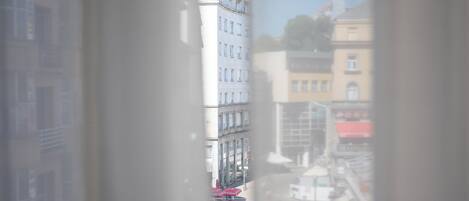 A view through a window of a multi-story building with balconies, a street with parked cars, and a clear sky.