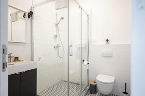Une salle de bain moderne avec une douche à parois de verre, des toilettes et un lavabo surmonté d’un miroir.