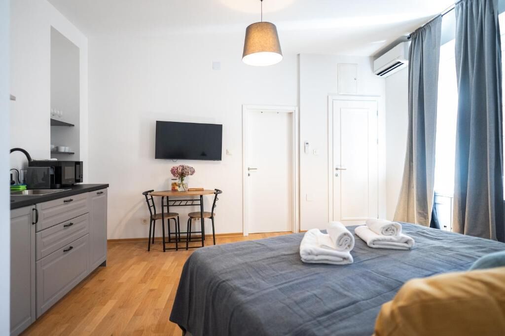 Une chambre d’hôtel moderne équipée d’un lit, d’un bureau avec une chaise, d’un téléviseur à écran plat et d’une kitchenette.