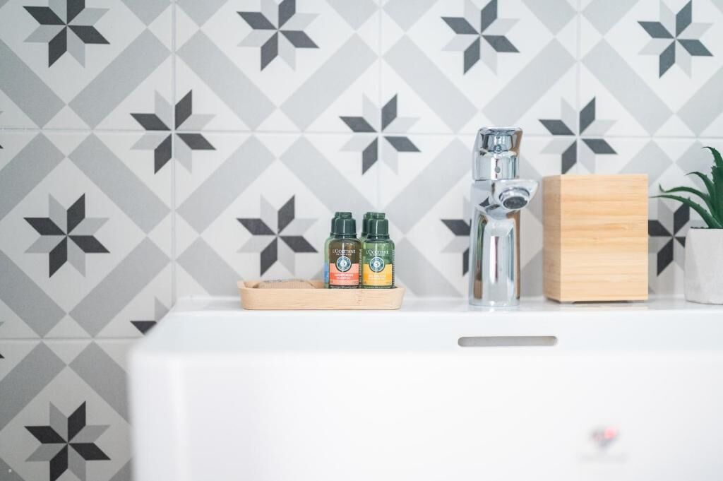 Un baño con un lavabo blanco, un grifo, una bandeja de madera con dos botellas y una planta en maceta.