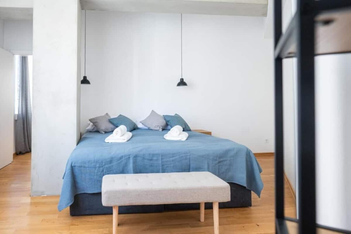 Un dormitorio con cama, almohadas, un banco y luces colgantes.