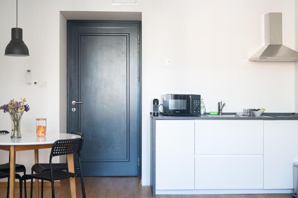 Une cuisine équipée d’un four à micro-ondes, d’une machine à café et d’un évier. On y trouve une porte avec une poignée et une petite table avec des chaises.