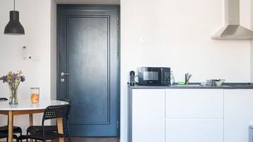 Una cocina con microondas, cafetera y lavabo. Hay una puerta con manija y una pequeña mesa con sillas.