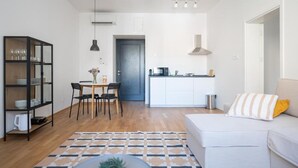 Een ruimtelijk ingerichte leefruimte met een eethoek, kitchenette en een bank met een gestreept kussen.