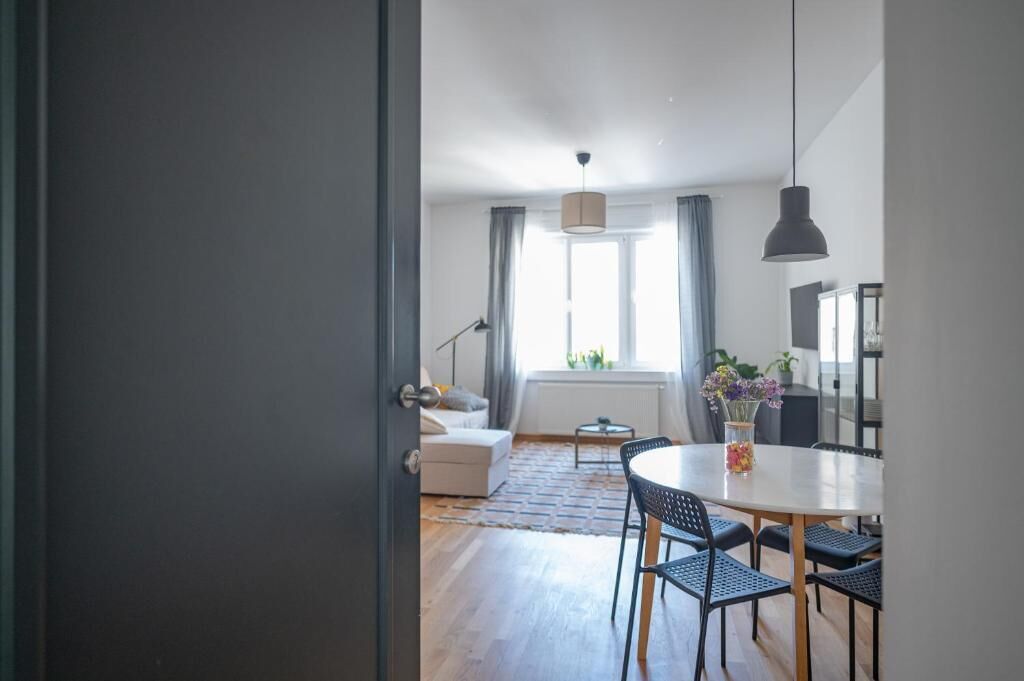 Una sala de estar moderna con un sofá, una mesa de comedor con sillas, una lámpara y un ventanal con cortinas.