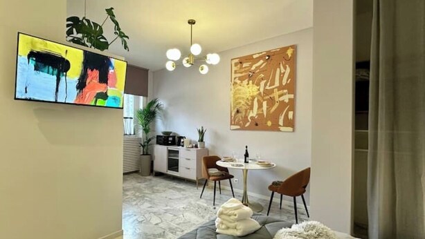Ein modernes Hotelzimmer mit einem großen Fernseher, einer Essecke und Kunstwerken an den Wänden.