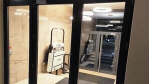 Hoteleingang mit Glastür, Gepäckwagen und einer im Hintergrund sichtbaren Treppe.