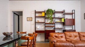 A living room with a glass dining table, wooden chairs, a brown leather sofa, and a bookshelf with various items. - Sonnino 17 Luxury Apartment (Cagliari)