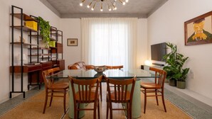 A dining area with a glass table, wooden chairs, a chandelier, a bookshelf, and a painting on the wall. - Sonnino 17 Luxury Apartment (Cagliari)
