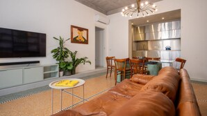 A living room with a leather sofa, a TV, a dining area with chairs, and a kitchen visible through an open door. - Sonnino 17 Luxury Apartment (Cagliari)