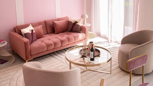 Un salon décoré dans des tons roses, avec un canapé, deux fauteuils, une table basse et une lampe.