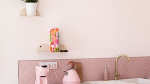 Une cuisine avec un plan de travail blanc, des appareils roses et des chaises dorées.