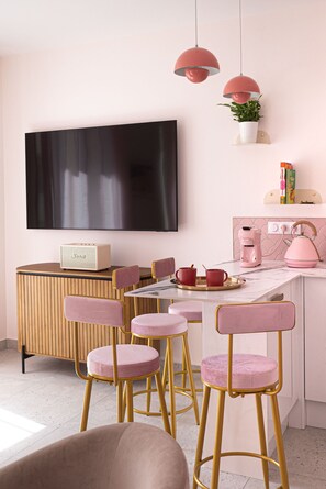 A modern kitchen with pink and gold accents, a flat-screen TV, and a coffee machine. - Rosa Vida • 2 Stylish BRs • Walk to Beaches & Croisettes (Cannes)