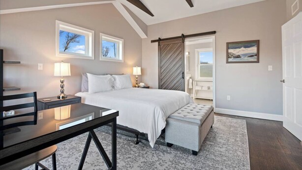 Quarto com cama, mesas de cabeceira, escrivaninha e um banco.