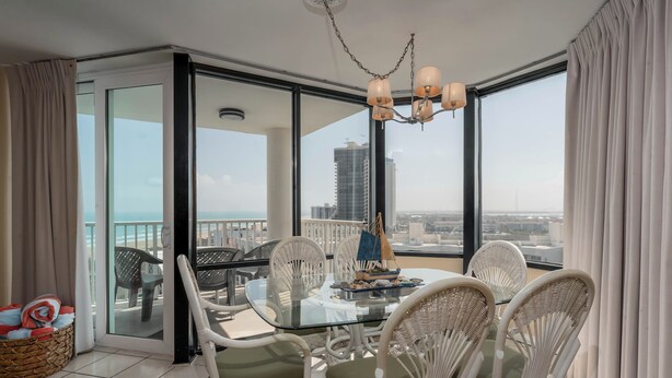 A balcony with a glass door, wicker chairs, a glass table, and a chandelier. - Saida Royale 145 - Premier Location with Breathtaking Ocean Views. The Only Thing Missing is You! (South Padre Island)