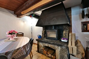 A stone fireplace with a black hood, a table with a patterned tablecloth, and a chair.