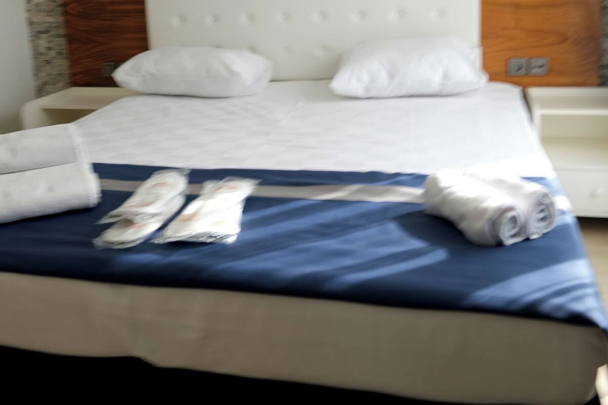 A hotel room with a bed, white pillows, a blue bedspread, and a wooden headboard.