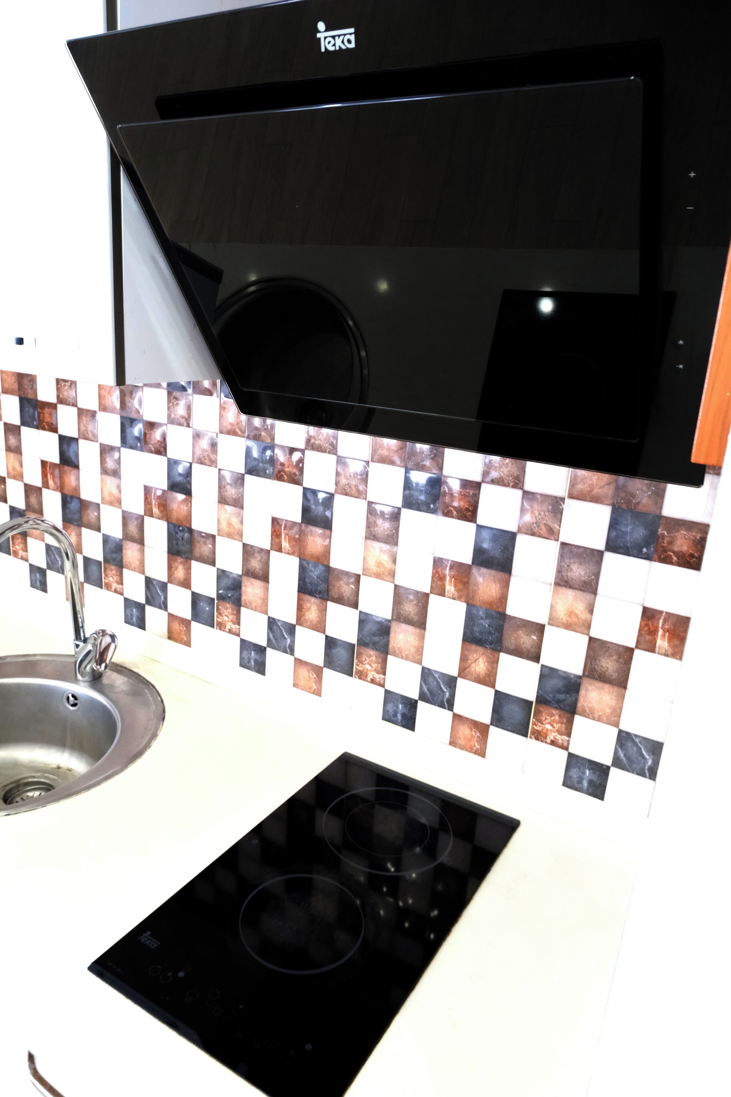 Una cocina con extractor de aire negro, salpicadero a cuadros, un lavabo de acero inoxidable y una placa de inducción negra.