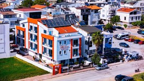A multi-story hotel with a rooftop solar panel array, a central entrance, and a parking lot with several cars.
