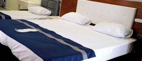 Una cama doble con colcha blanca y azul, cabecera de madera y un equipo de aire acondicionado en la pared.