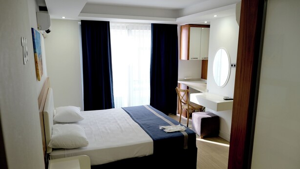 A hotel room with a bed, a desk, a chair, a mirror, and a window with curtains.