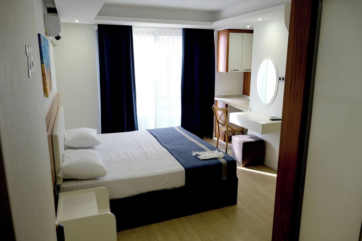 A hotel room with a bed, a desk, a chair, a mirror, and a window with curtains.