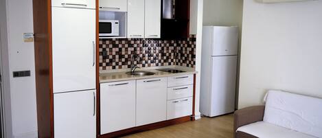 A compact kitchen with white cabinets, a microwave, a sink, and a refrigerator.