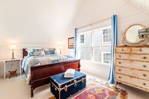 Un dormitorio con cama, cómoda, ventana y maleta.