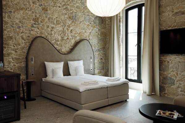 A bedroom with a stone wall, a bed with white linens, a bedside table, and a television on the wall.