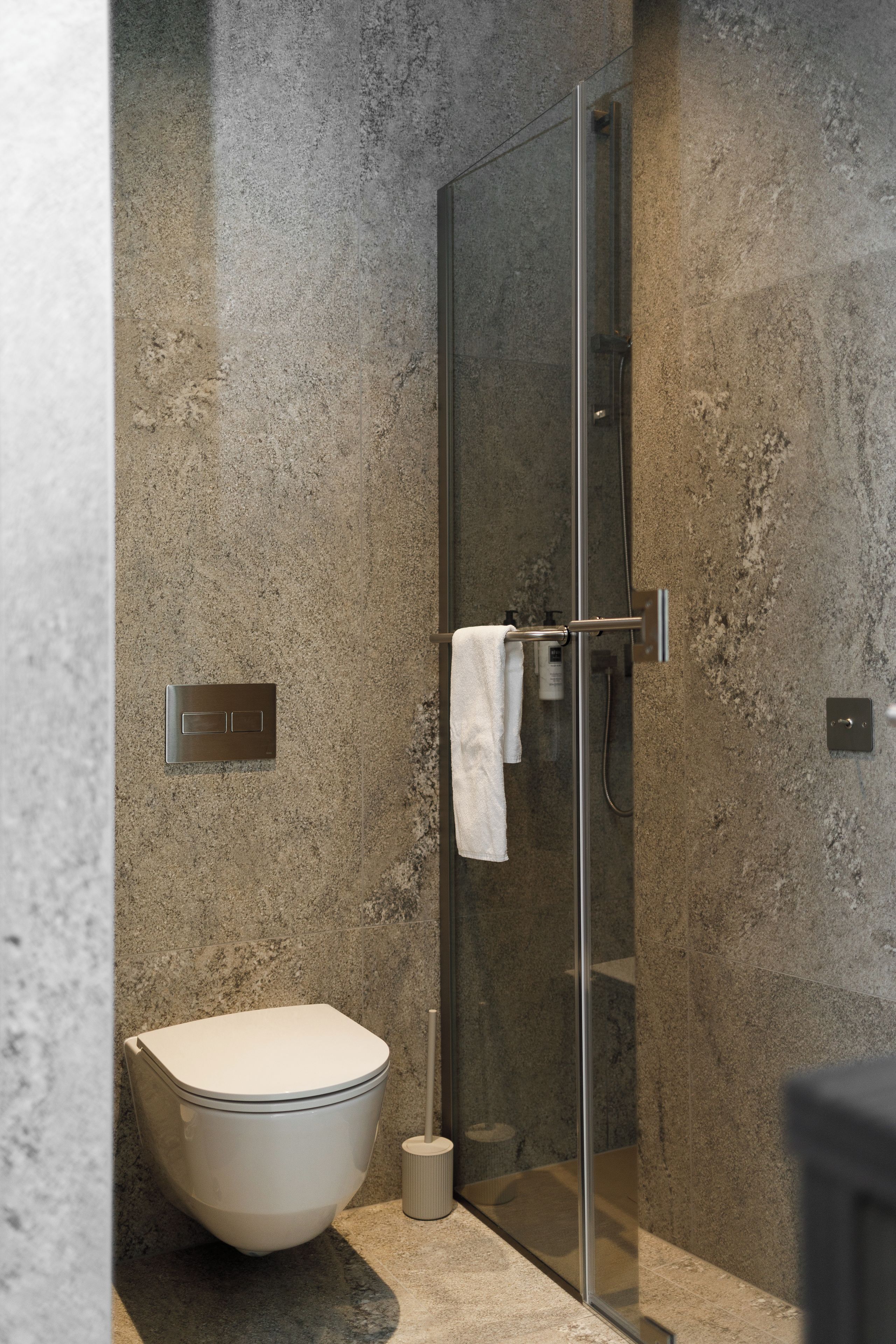 A modern bathroom with a glass-enclosed shower, a standalone toilet, and a towel rack.