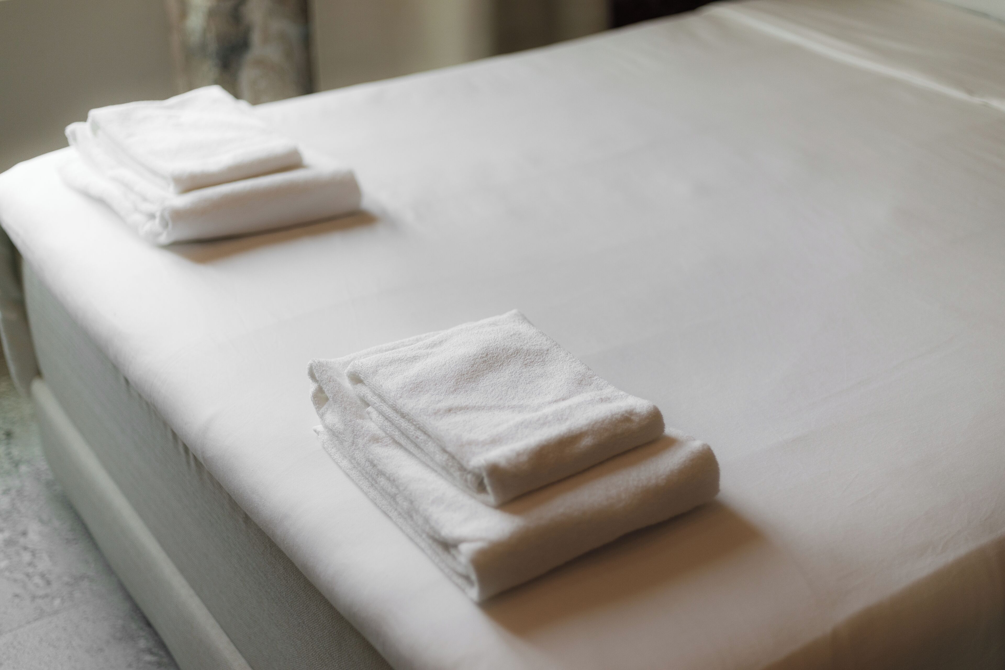A neatly made bed with white linens and two folded towels on the side.