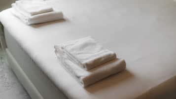A neatly made bed with white linens and two folded towels on the side.