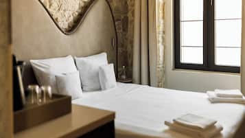 Une chambre d’hôtel avec un mur en pierre, un lit avec du linge de maison blanc, une table de chevet en bois et une fenêtre avec des rideaux.