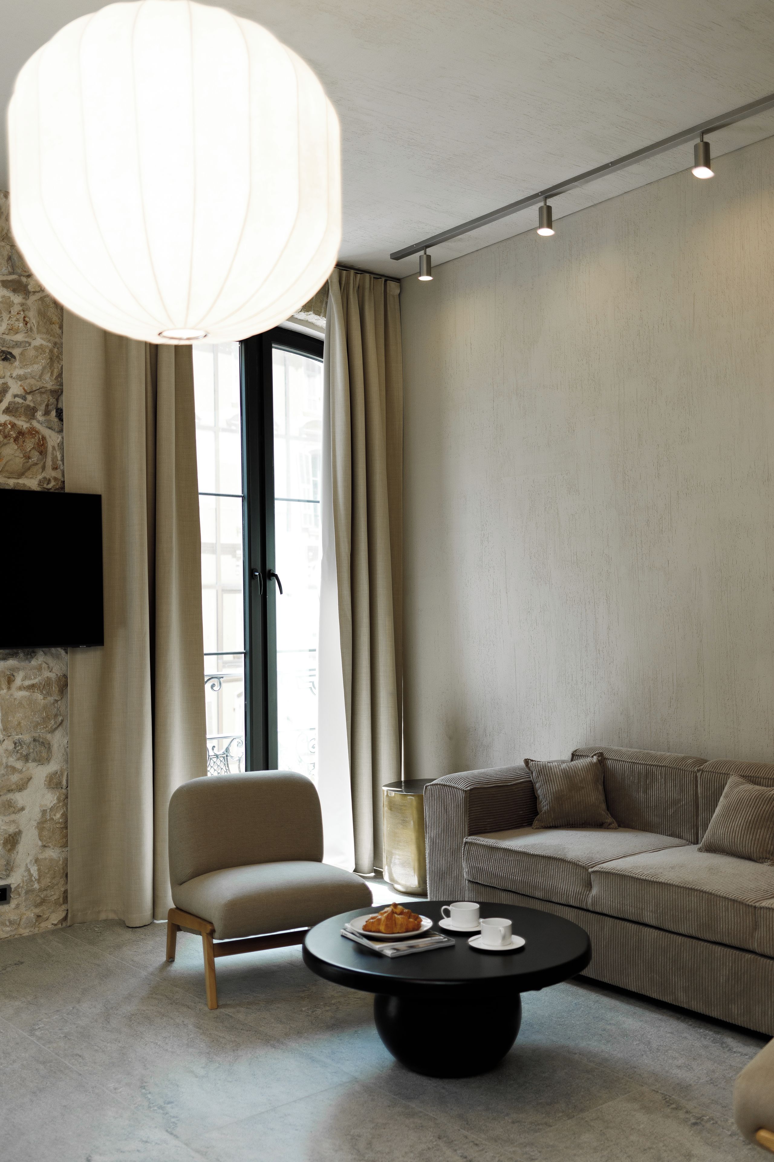 Ein modernes Wohnzimmer mit einer Couch, einem Sessel, einem Couchtisch und einem an einer Steinwand befestigten Fernseher.