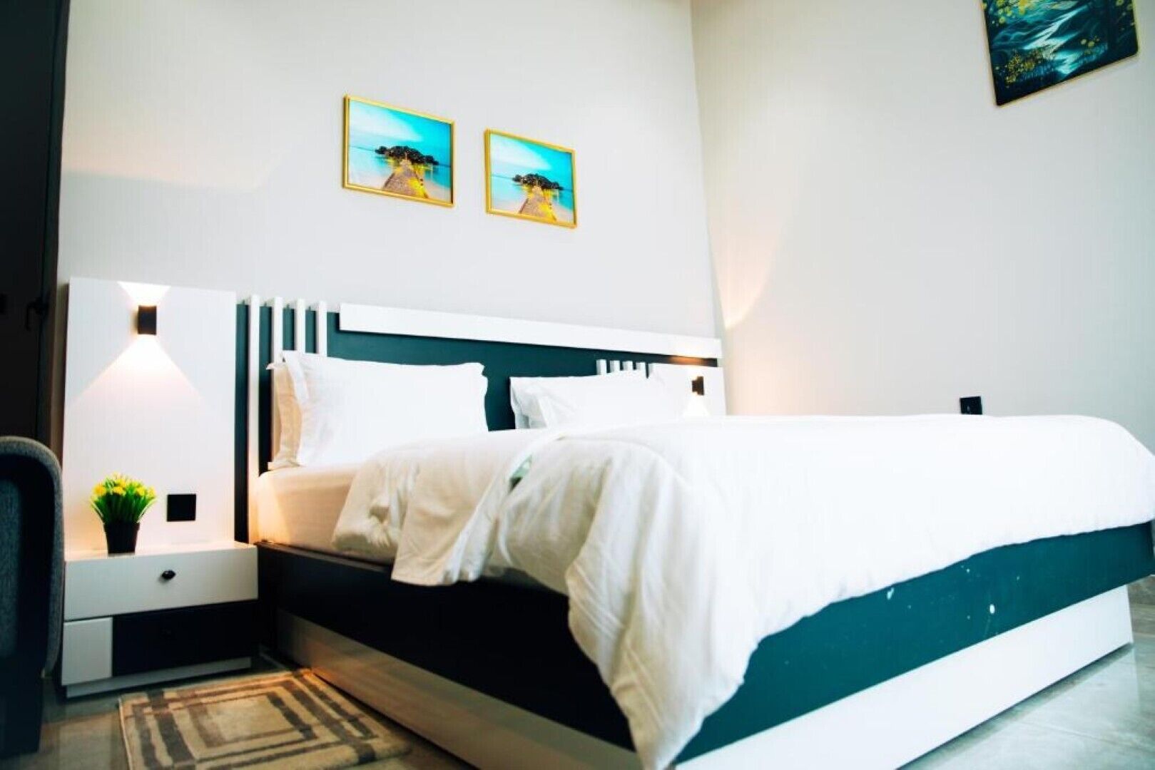 Een moderne slaapkamer met een bed, nachtkastjes en twee aan de muur hangende foto’s.