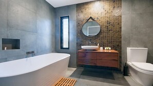 A modern bathroom with a freestanding bathtub, a wooden vanity, a round mirror, and a toilet.