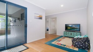 A modern living room with a sliding glass door, a television on a cabinet, and a patterned rug. - KK s in Lennox Head - Moments to the Ocean (Lennox Head)