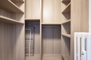 Un vestidor con estantes de madera, un tendedero de metal y un radiador.