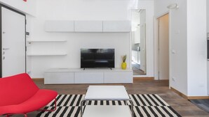 Un salon moderne avec un téléviseur à écran plat, un fauteuil rouge, une table basse blanche et un tapis à rayures.