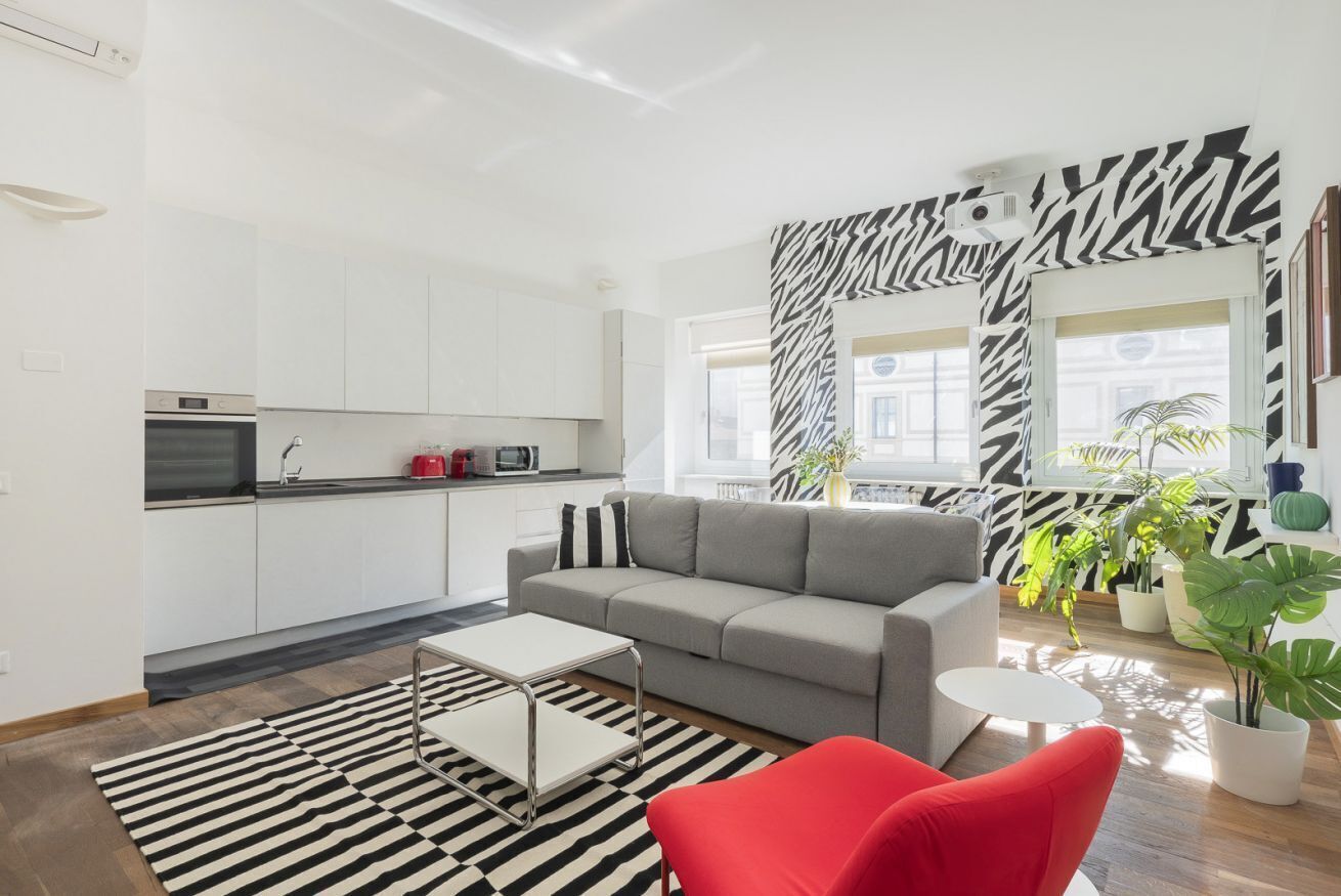 Un appartement moderne comprenant une cuisine, un canapé gris, un fauteuil rouge et un mur orné d’un motif zébré.