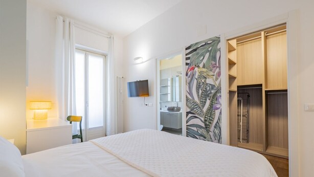 Une chambre d’hôtel avec un lit, une télévision, une armoire et une salle de bain visible à travers une porte ouverte.