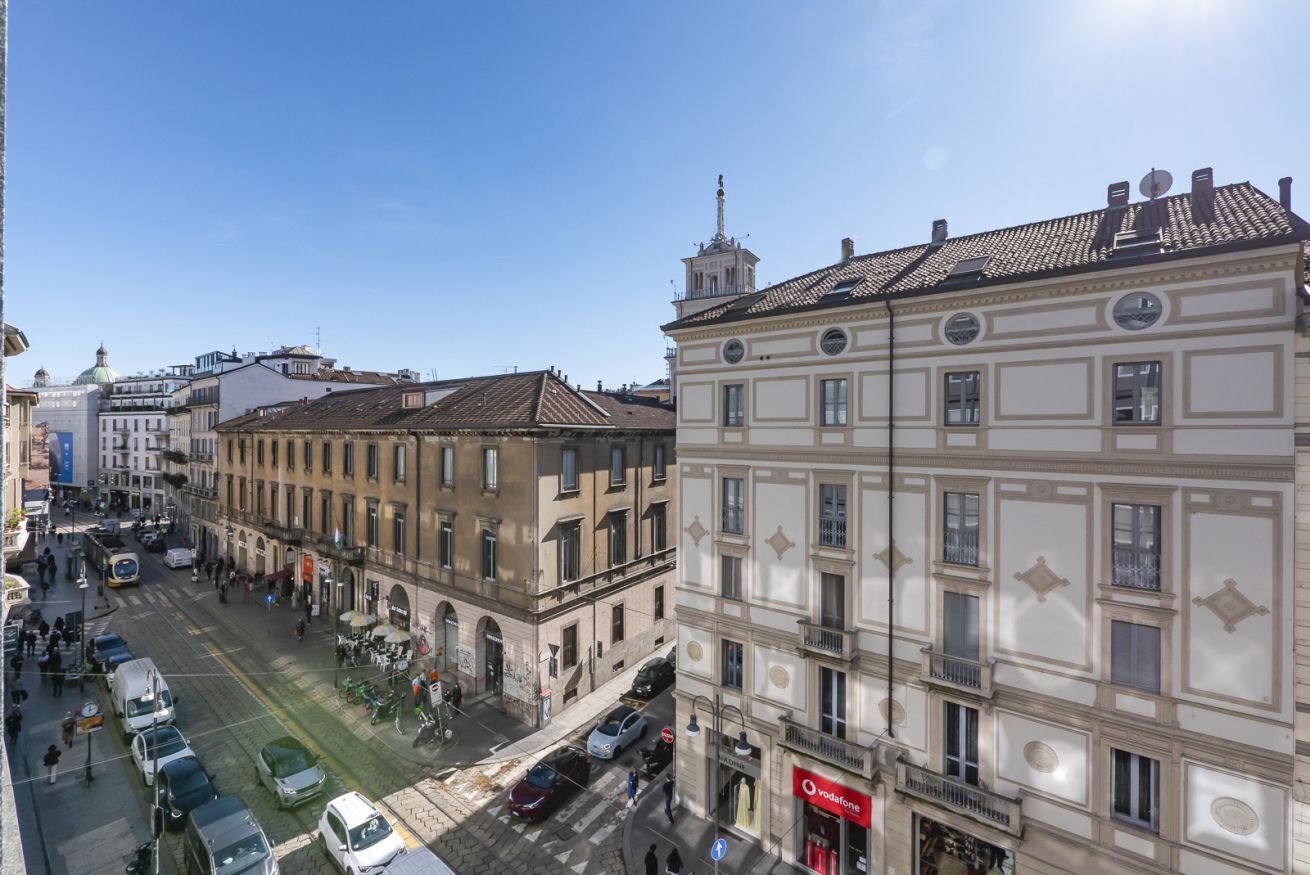 A street view with buildings, a clear sky, and parked cars.