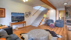 A living room with a TV, sofa, ottoman, and a staircase.